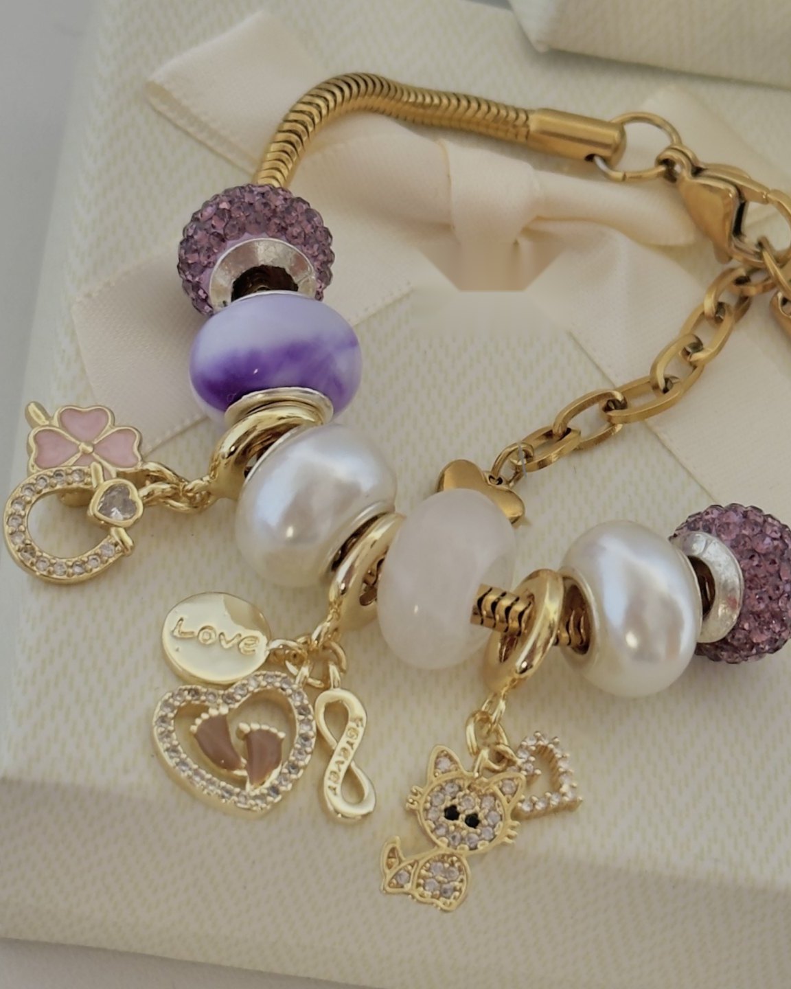 Pulsera dorada con cuentas lila, perlas, cuarzo y charms de trébol, corazón, infinito y gatito
